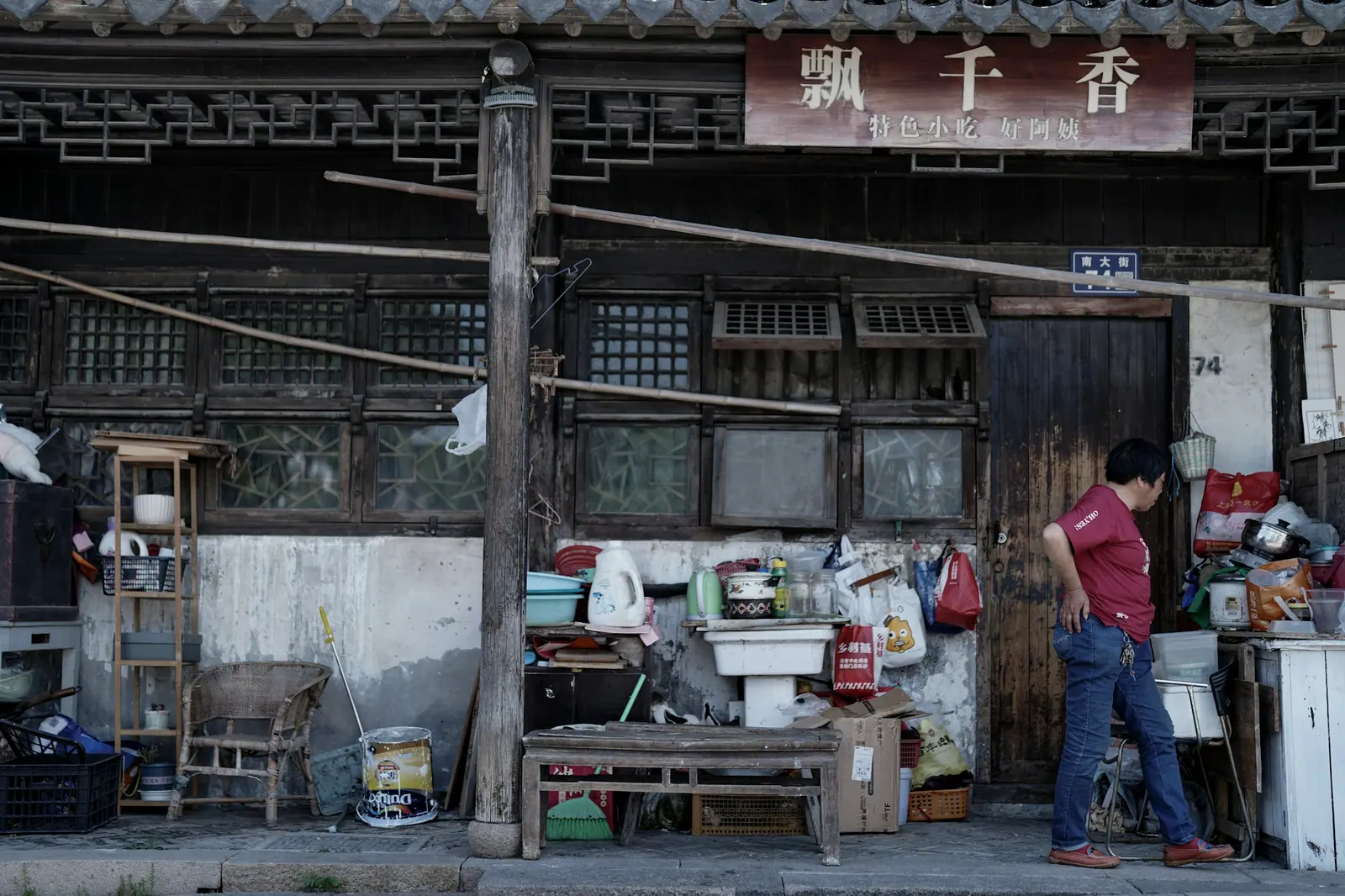 一个人站在杂物堆满的老屋门口,招牌上写着店名