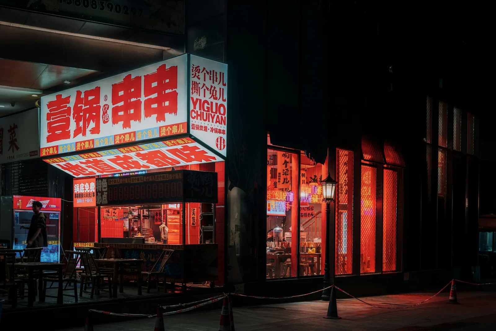 夜里的一间串串店,白底红字的招牌在黑暗的街边发亮