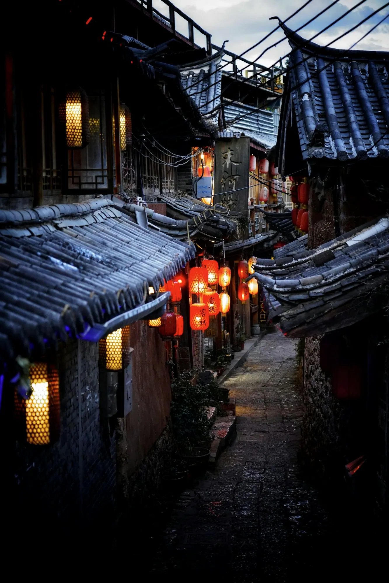 一条窄窄的石板巷,两边是青瓦屋檐,红灯笼已经亮了